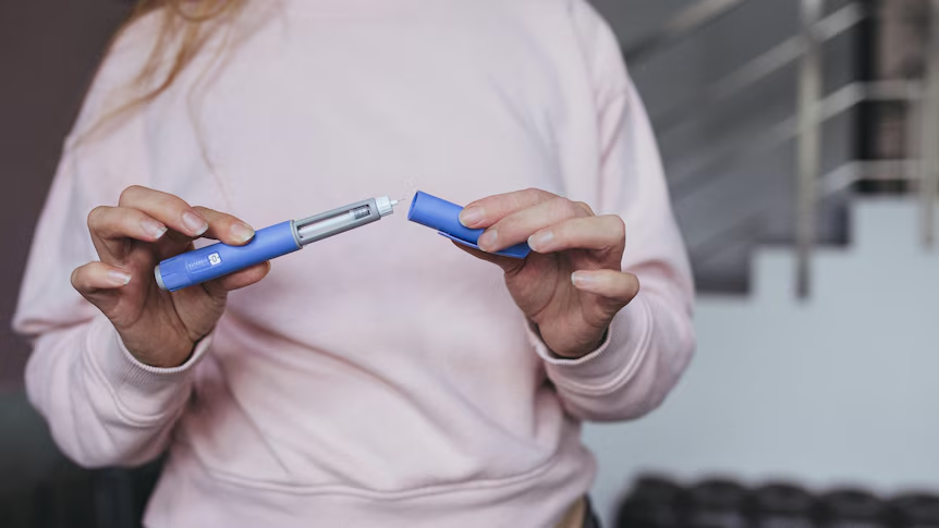 Person holding a blue insulin injection pen with cap removed.
