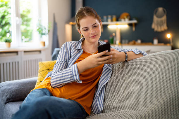Young woman relaxing on a gray sofa using her smartphone at home.