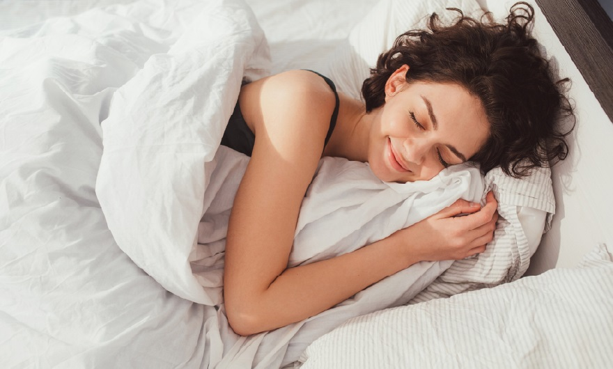 Woman with curly hair smiling peacefully while sleeping in white bedding.