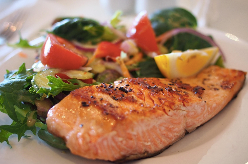 Grilled fish on a plate with tomatoes and green vegetables.