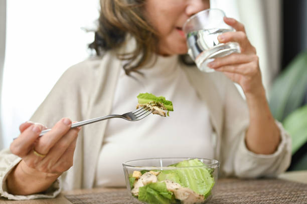 A woman eats a green salad with a fork while drinking a glass of water.
