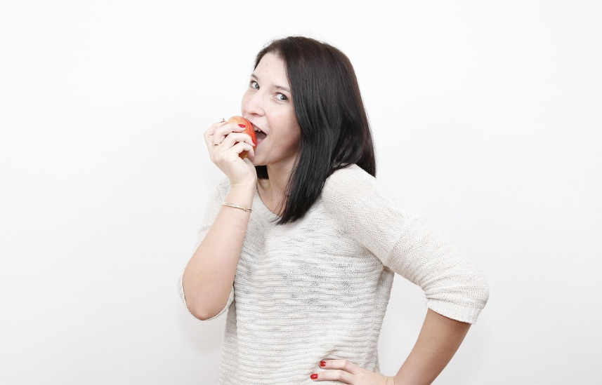 A woman smiling and biting into an apple.