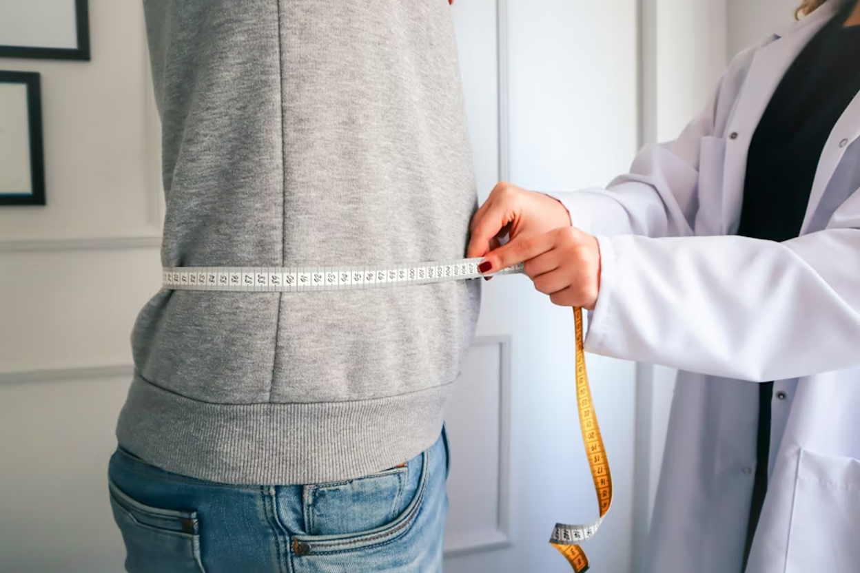 Healthcare professional in a white coat measuring a patient's waist with a tape measure during a clinical consultation