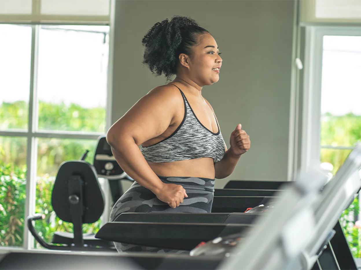 Woman in athletic wear running on a treadmill in a bright gym with large windows overlooking greenery