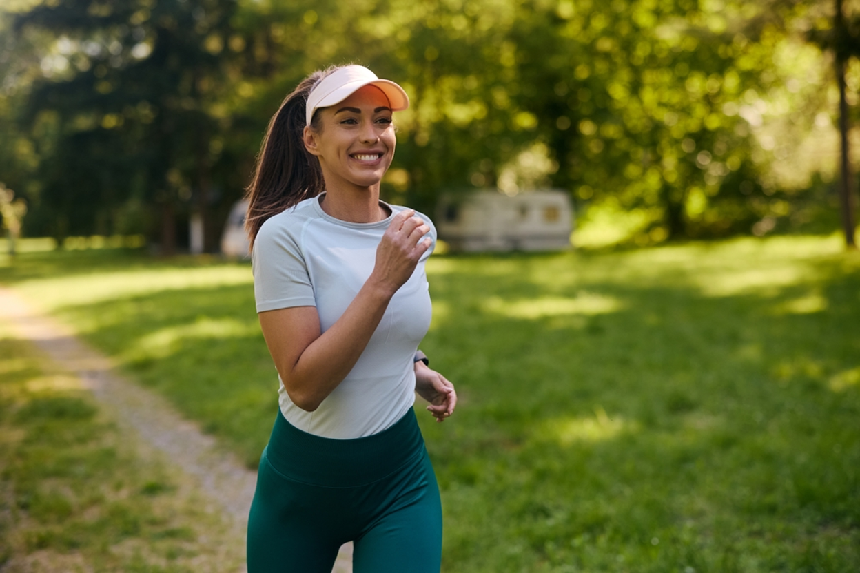 Woman jogging outdoors on a sunny park trail surrounded by trees