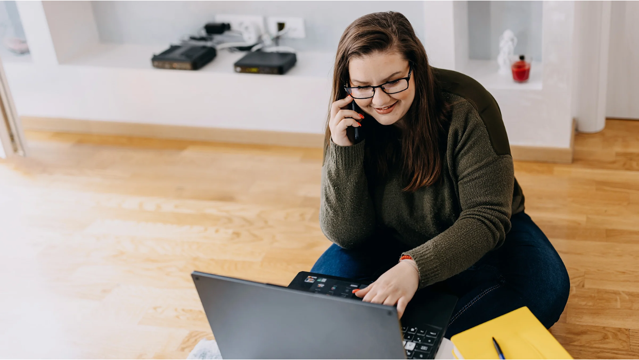 Woman on a phone call and laptop at home, representing the ease of consulting a telehealth provider for a GLP-1 prescription online