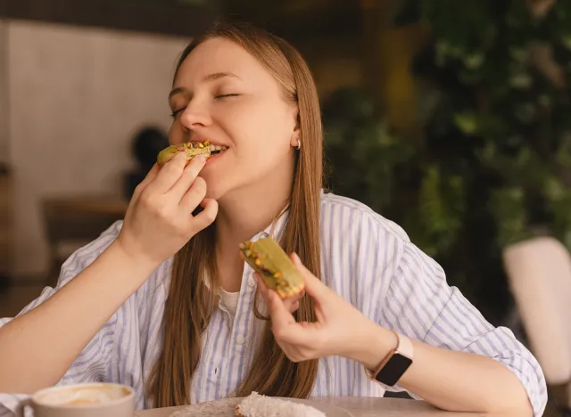 Woman in striped shirt smiling while eating a sandwich outdoors.