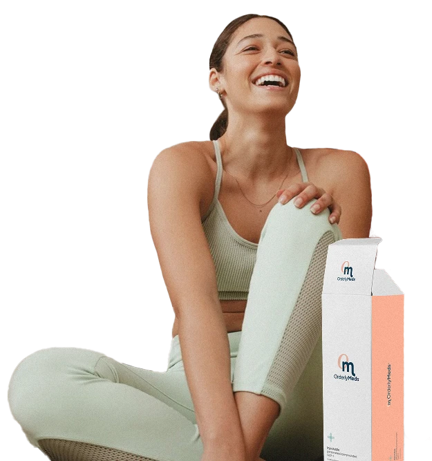 Smiling woman in sage green athletic wear sitting cross-legged next to OrderlyMeds product packaging against a black background."
