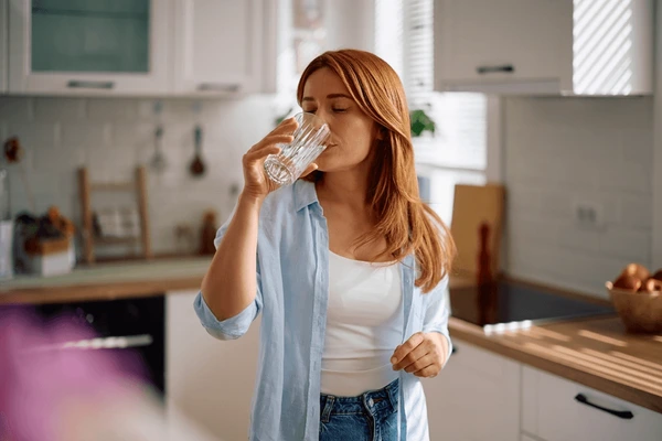 Woman drinking a glass of water in a bright, modern kitchen.